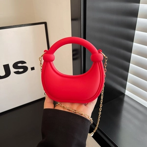 Red mini half-moon crossbody bag with gold chain strap and ring handle held by hand