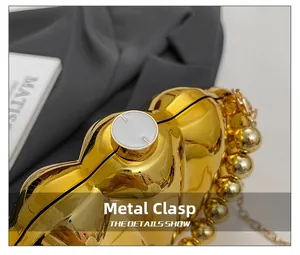 Detail of golden shell-shaped clutch featuring metal clasp and beaded handle chain
