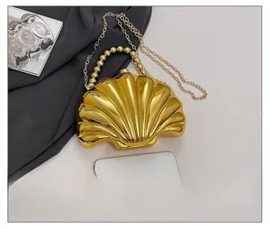Golden shell evening bag with pearl handle and chain strap shown next to a smartphone