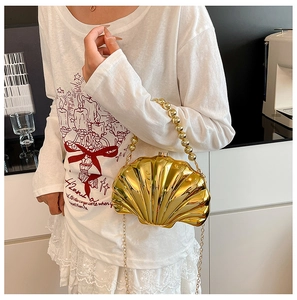 Mini golden shell-shaped clutch bag with beaded handle and chain strap on a model