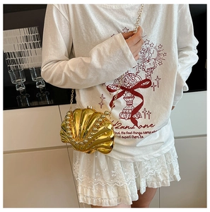Detailed shot of golden shell-shaped mini bag with white pearl trim and a metallic chain