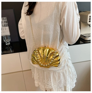 Detail of a shiny gold shell-shaped bag with pearl accents and a chain strap