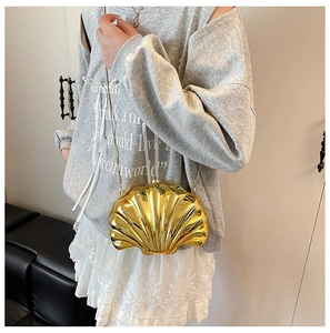 Detail shot of mini gold shell-shaped clutch with metal chain on model outfit