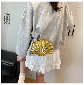 Close-up of a golden shell-shaped crossbody bag with metal chain strap on a model