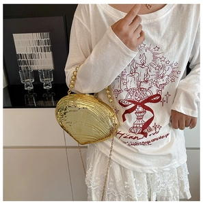 Detail of golden shell-shaped acrylic clutch bag with bead handle and metallic texture