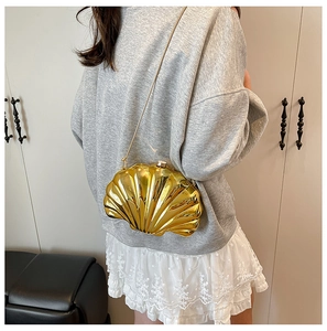 Golden shell-shaped mini chain bag shown as a crossbody on a model in a modern home setting