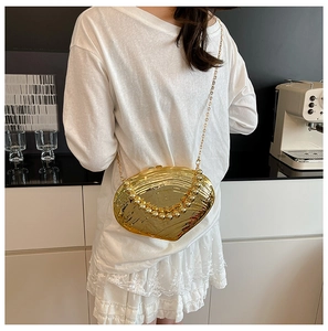 Detail of gold seashell evening bag with wave texture and beaded handle on a white model