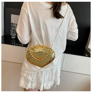 Detail of a shiny gold heart-shaped evening bag with pearl handle and metal chain strap