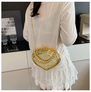 Golden seashell acrylic clutch bag shown on model with pearl handle and chain strap