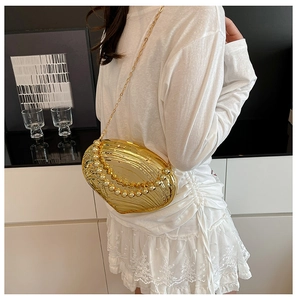 Detail of golden shell-shaped evening clutch with pearl handle and metal chain strap