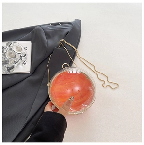 Detailed shot of spherical acrylic clutch with orange marble texture and gold chain strap