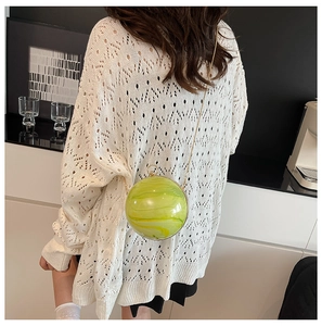 Detail of green and yellow marble ball bag with gold chain strap on a white knit outfit