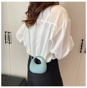 Detail of light blue acrylic mini handbag with gold chain strap shown on person