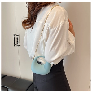 Detail of light blue crescent acrylic handbag with elegant gold metal chain strap