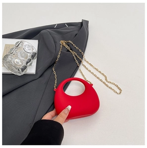 Detail of red crescent handbag with hollow handle and gold chain on grey blazer