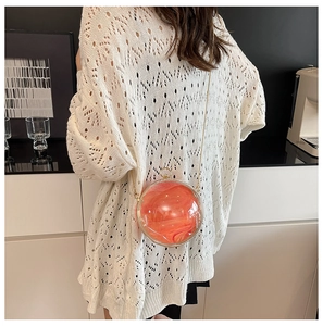 Close-up of a spherical acrylic evening bag with orange marble texture and gold chain