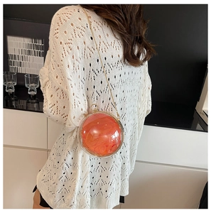 Close-up of a spherical acrylic evening bag with bright orange lining and gold chain strap