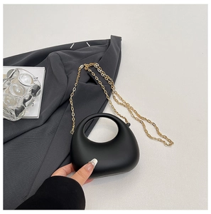 Detail of matte black handbag featuring a circular hollow handle and gold chain strap