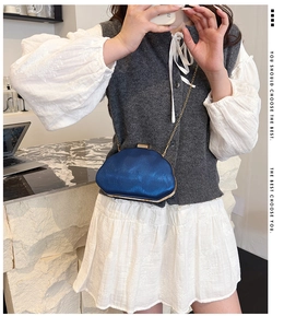 Detail of blue shell-shaped clutch featuring wave texture and golden chain strap