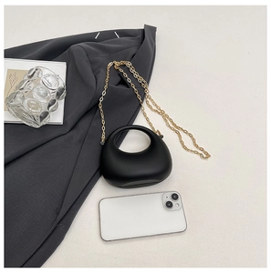Mini black acrylic handbag with gold chain strap and hollow handle next to a smartphone