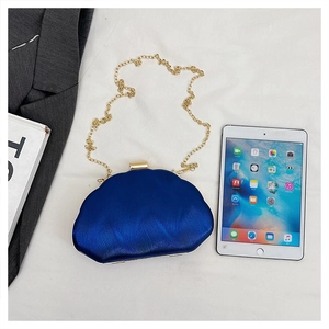Detail of blue shell pleated evening bag with gold chain strap on grey blazer background