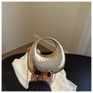 Macro shot of gold crescent moon evening bag with hammered metal texture and chain