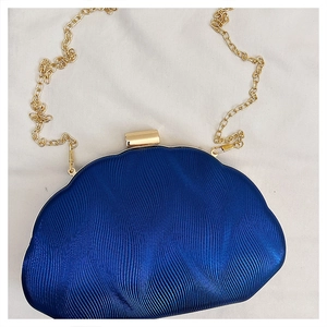 Detailed macro view of dark blue satin clutch featuring ripple texture and gold chain strap