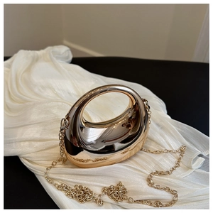 Detailed close-up of a crescent gold mirror evening bag on soft white silk background