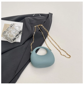 Detail of teal acrylic handbag with gold metal chain on a textured surface