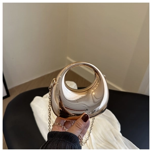 Close-up of golden crescent evening bag with mirror finish and circular hollow handle