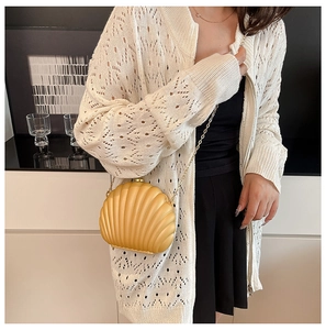 Close-up of shell-shaped crossbody bag with gold chain strap on a knit sweater