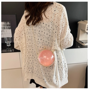 Detail showing a pink spherical chain bag worn crossbody over a white knit top