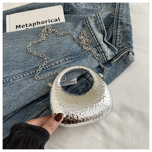 Detail of silver crescent mini bag with hammered metallic texture and silver chain strap
