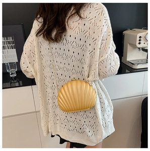 Detailed view of bright yellow shell-shaped acrylic clutch bag with a fine gold chain strap