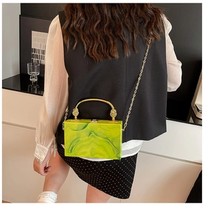 Detail of green and yellow marble acrylic box bag with gold handle on a model