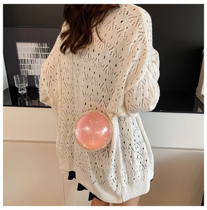 Detail shot of a round pink acrylic sphere bag with a gold metal chain on a model
