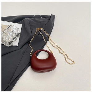Detail of wine red semi-circular crossbody bag with fine gold metal chain strap