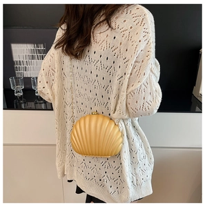 Detailed view of the seashell clutch bag with matte texture and gold chain on a model