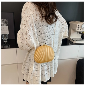Shell-shaped evening clutch bag with gold chain strap worn over white knit cardigan