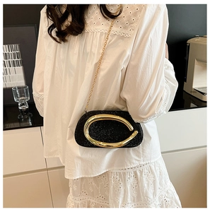 Close-up of a glossy black evening clutch with a bold gold oval handle and chain strap