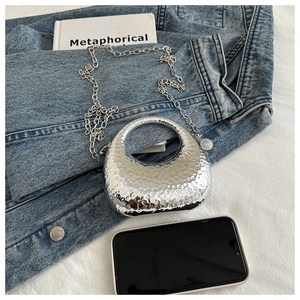 Detail of silver crescent handbag featuring hammered texture and circular handle
