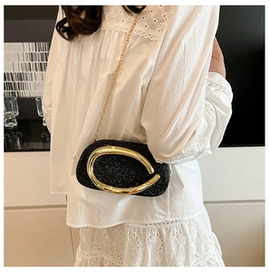 Detail of a black glitter clutch bag with a golden ring clasp and metal chain strap