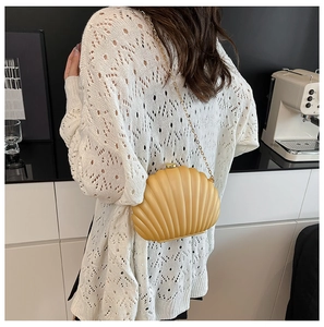 Close-up of shell-shaped mustard yellow clutch with gold metal chain on a model