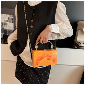 Detail of orange marble acrylic box bag with golden curved handle and chain strap