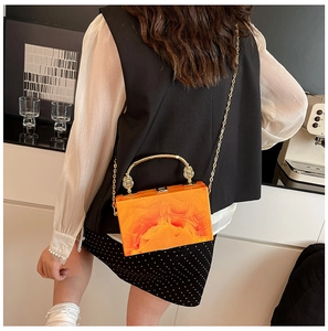 Detail of orange marble acrylic box bag with gold metal handle and chain strap