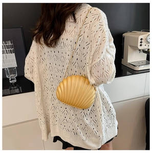 Detail of cream yellow shell-shaped acrylic bag with gold chain strap in lifestyle setting