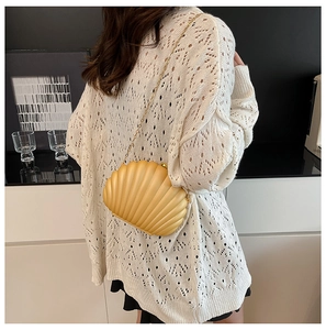 Detail of yellow shell clutch bag with gold chain strap on white crochet sweater