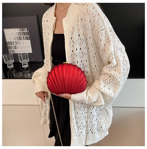 Detail of red shell-shaped evening clutch with gold chain strap on female model