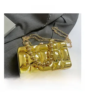 Detail of gold metal clutch bag with embossed texture, round bead handle and chain strap