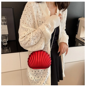 Detailed view of red shell-shaped crossbody bag with gold chain strap on model